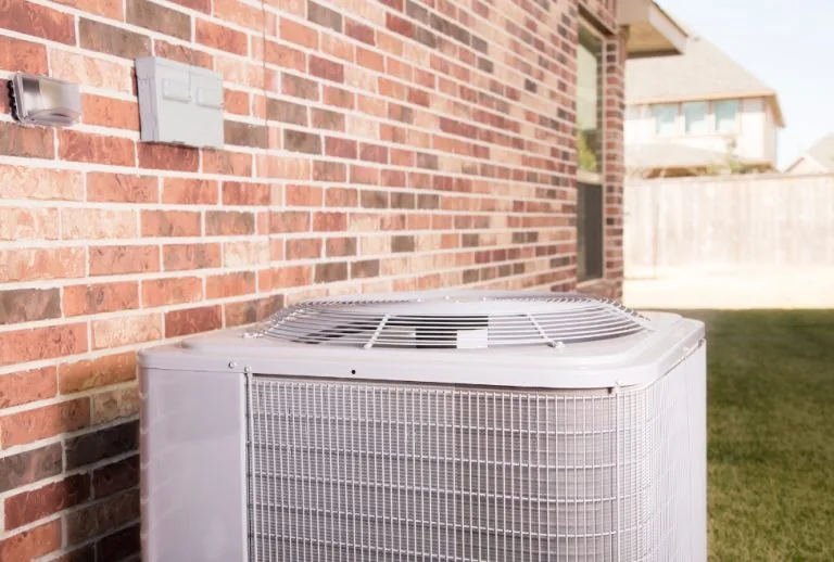 Air conditioner outside a home in a residential neighborhood during summer with potential AC drain line clog issues bein