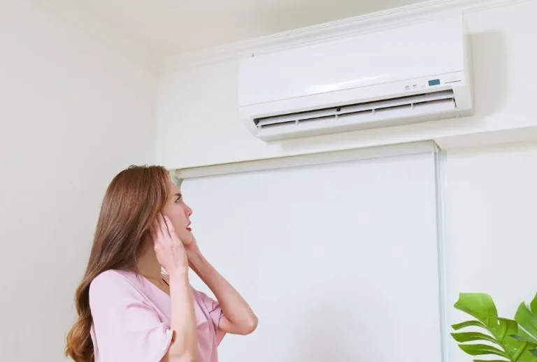 Woman covering her ears next to a noisy air conditioner in a residential home, highlighting common issues like strange A