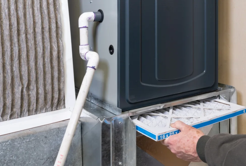 A man replacing a dirty furnace filter in a home to ensure efficient heating and safety during winter