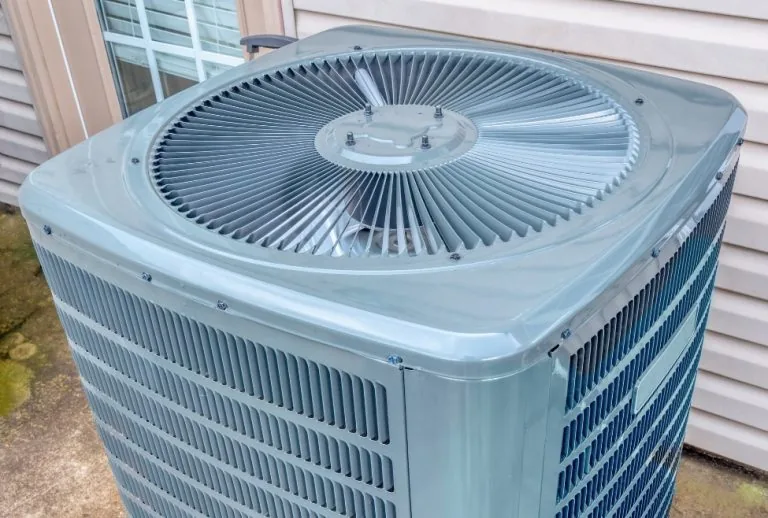 An outdoor air conditioning unit installed behind a residential home, highlighting common signs of aging or inefficiency