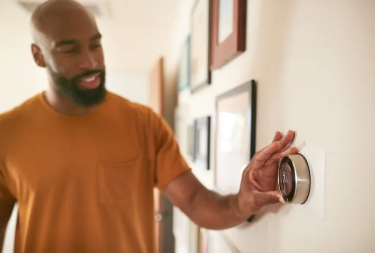 A man adjusting a digital thermostat to optimize heating at home, showcasing energy-saving techniques for reducing winte