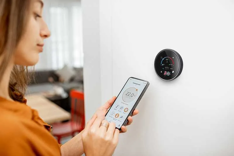 A woman using her phone to control a smart thermostat from Paradise Heating and Air, showcasing advanced thermostat technology for energy-efficient temperature control and smart home integration