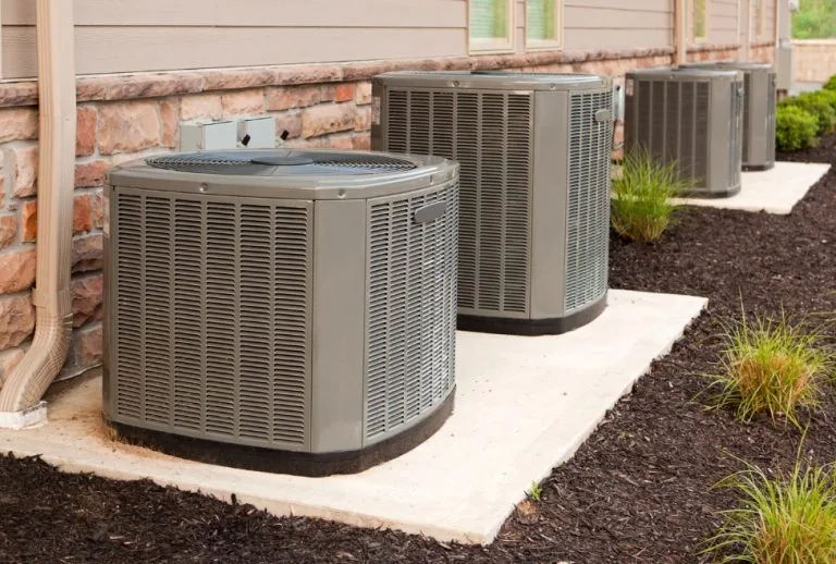 Multiple outdoor air conditioning units behind a residential or commercial building, representing common HVAC issues lik