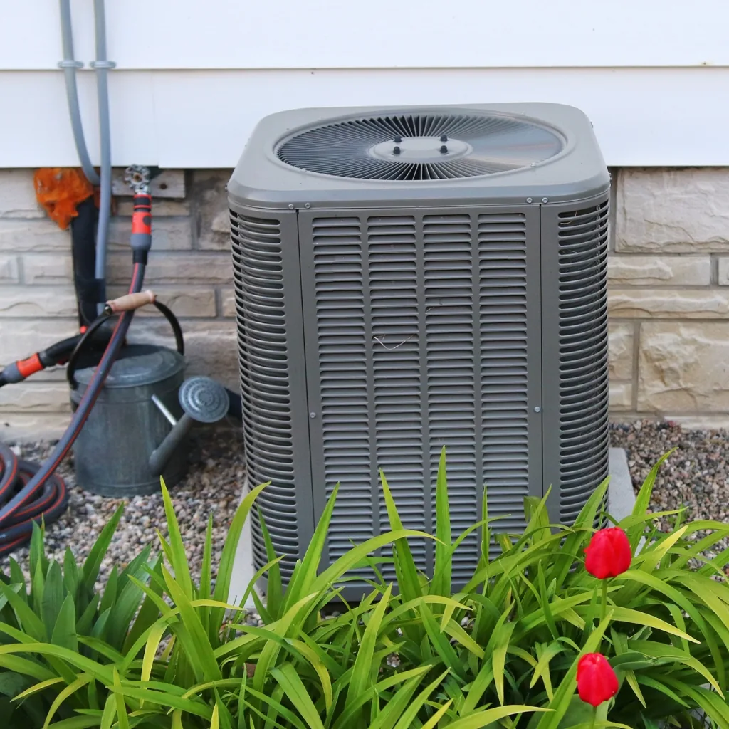Outdoor residential air conditioner with red flowers in front