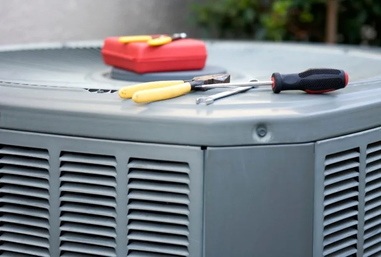 Air conditioner with tools on top outside a home, representing common AC repair issues like refrigerant leaks, capacitor