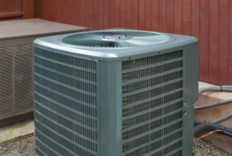 Residential air conditioner unit outside a home, highlighting importance of AC drain line cleaning, preventing clogs and