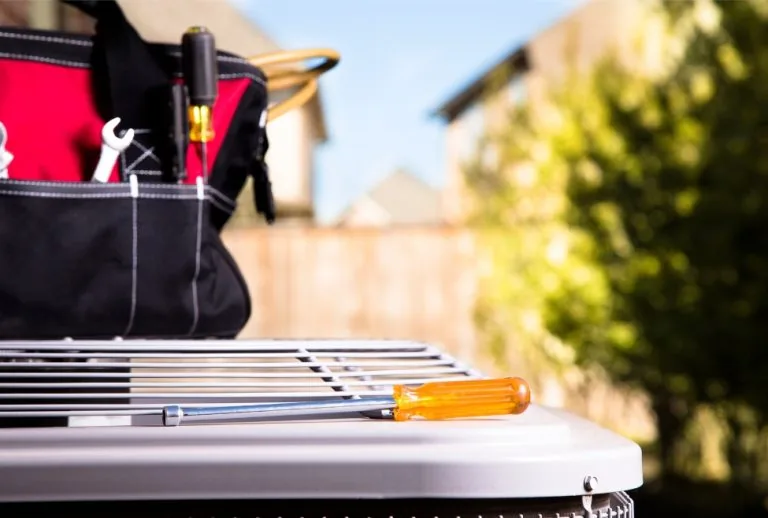 HVAC technician tools placed on an outdoor air conditioner unit during AC filter replacement service — representing rout