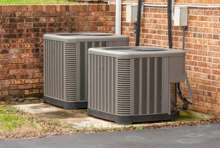 Two commercial air conditioning units outside a brick building, illustrating potential overheating issues, AC repair nee