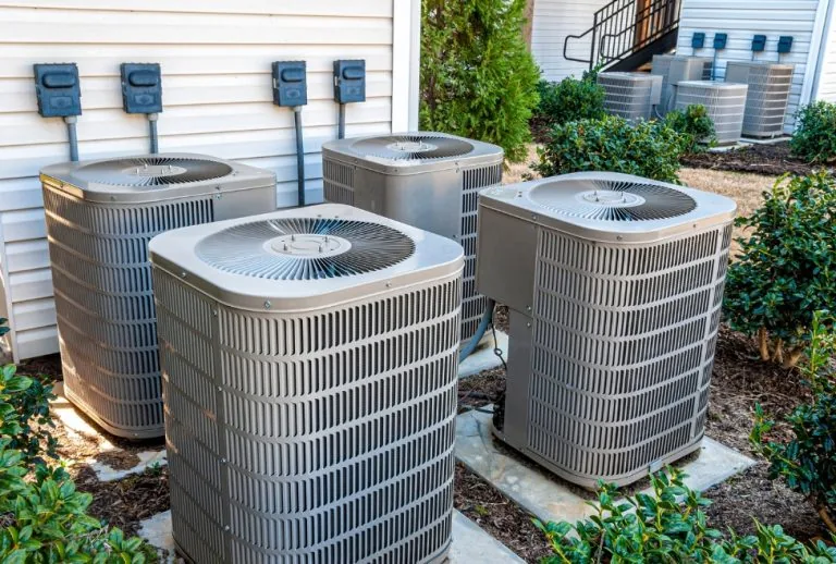 Multiple outdoor AC units behind an apartment building, highlighting potential HVAC issues like a bad fan motor, common 