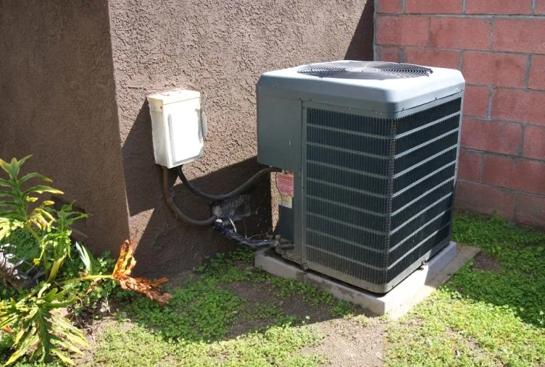 Outdoor residential air conditioner with fan not spinning, possible signs of AC capacitor failure, motor issues, or cool