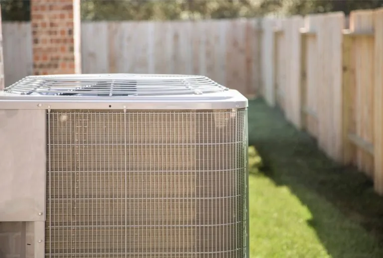 Close-up of an outdoor air conditioner unit next to a wooden fence at a residential home, representing common HVAC issue